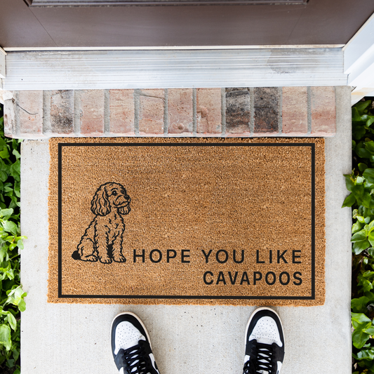 Hope You Like Cavapoos coir doormat with a drawing of a sitting Cavapoo in front of a brick step, top-down view with sneakers