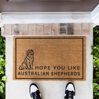 Hope You Like Australian Shepherds coir doormat with a drawing of a sitting Australian shepherd in front of a brick step, top-down view with sneakers