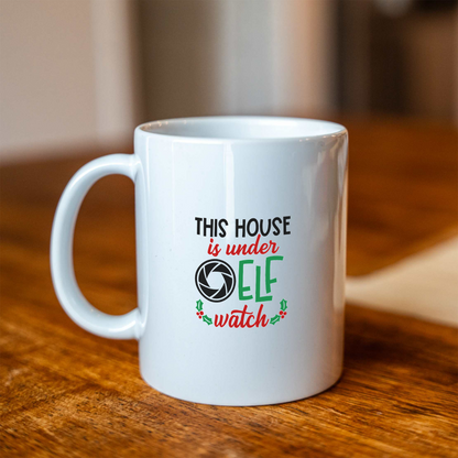 This House Is Under Elf Watch white ceramic Christmas coffee mug on a wooden table