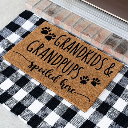 Grandkids & Grandpups Spoiled Here coir doormat with paw prints at an angle on a black and white buffalo check rug