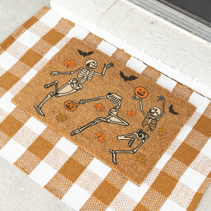 Dancing skeletons Halloween coir doormat on a tan and white check rug