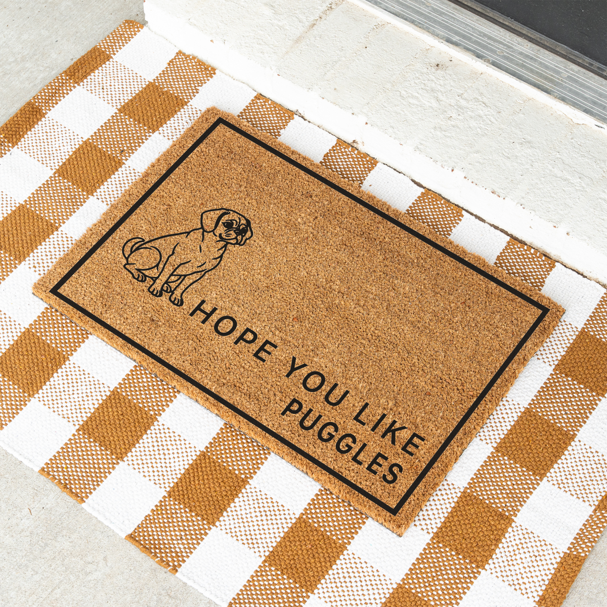 Hope You Like Puggles coir doormat with a drawing of a sitting Puggle at an angle on a tan and white check rug