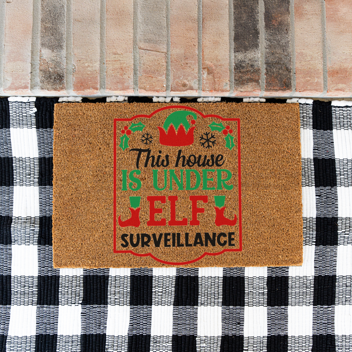 This House Is Under Elf Surveillance framed coir doormat on a black and white buffalo check rug at a brick step