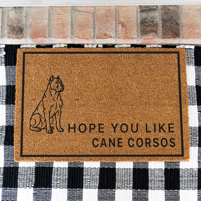 Hope You Like Cane Corsos coir doormat with a drawing of a sitting Cane Corso on a black and white buffalo check rug, close view