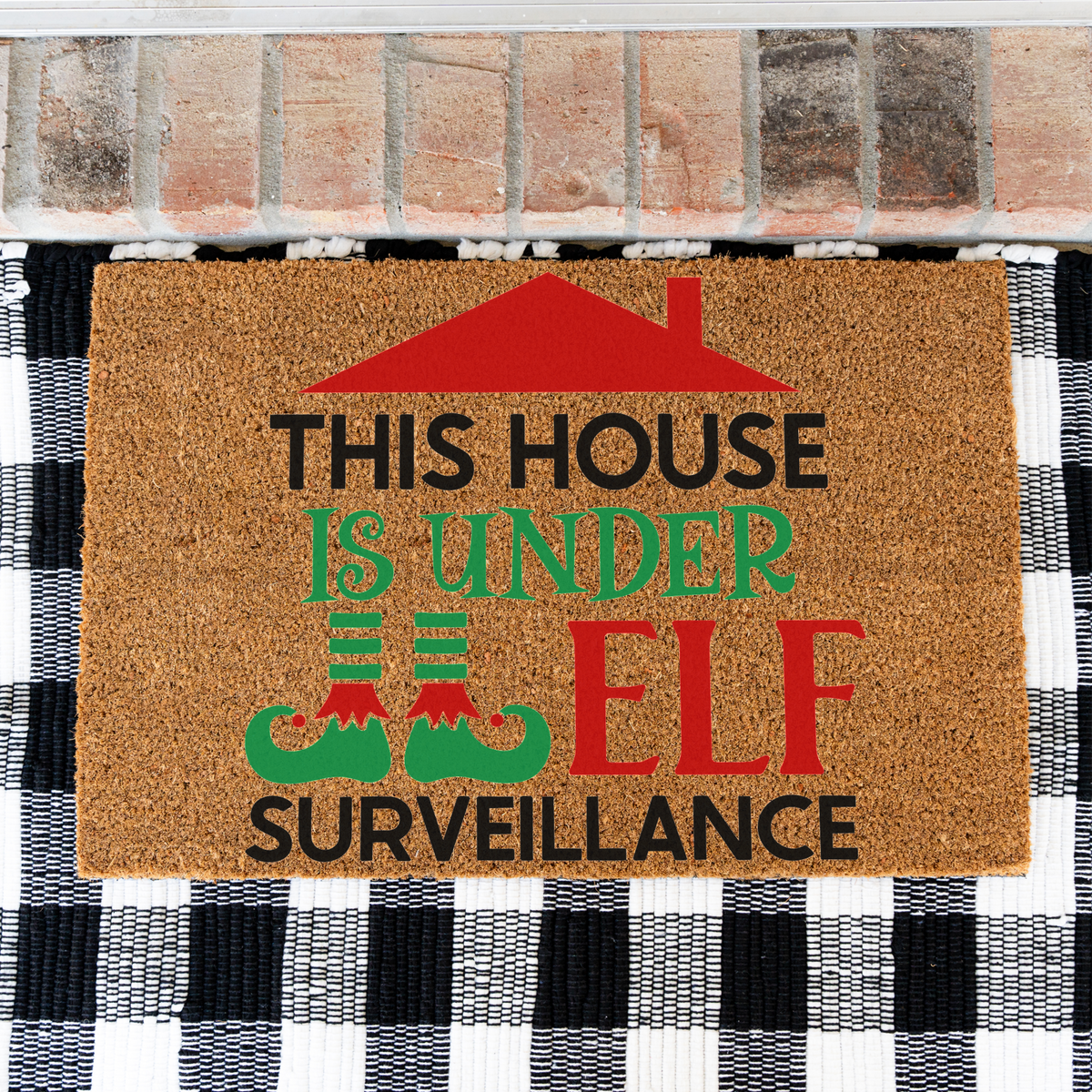 This House Is Under Elf Surveillance coir doormat on a black and white buffalo check rug, close view