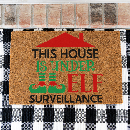 This House Is Under Elf Surveillance coir doormat on a black and white buffalo check rug, close view