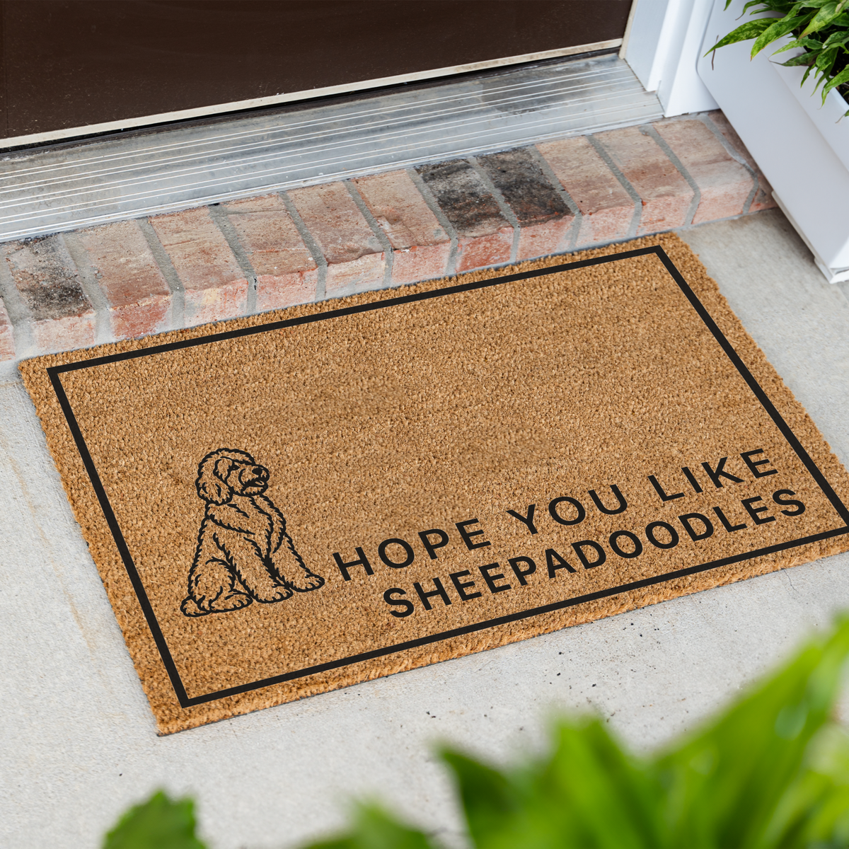 Hope You Like Sheepadoodles coir doormat with a drawing of a sitting Sheepadoodle at an angle on a front porch by a brick step