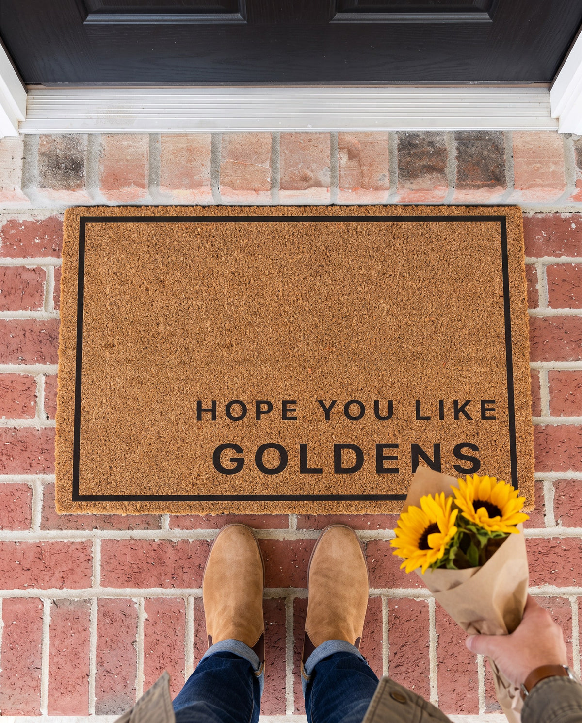 Hope You Like Goldens minimalist coir doormat on a brick stoop with a guest holding sunflowers