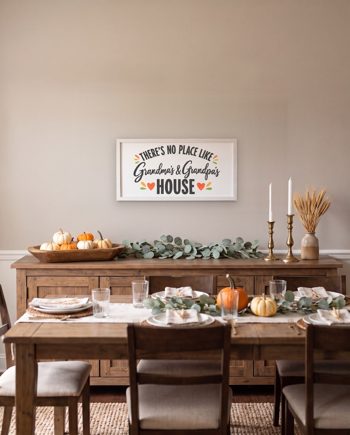 There's No Place Like Grandma's & Grandpa's House wide framed sign with a white frame, shown in 36x18, hanging above a dining room sideboard with fall decor