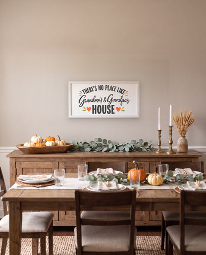 There's No Place Like Grandma's & Grandpa's House wide framed sign with a white frame, shown in 36x18, hanging above a dining room sideboard with fall decor